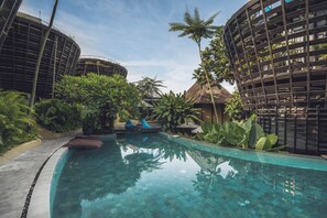 Zona de piscina amb superfície d'aigua cristal·lina, envoltada de vegetació abundant i arquitectura moderna.