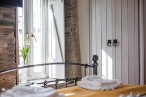 Un lit avec une tĂȘte de lit en bois, une fenĂȘtre donnant sur un mur de pierre et une porte avec un cadre blanc.