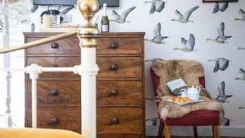 A bedroom with a wooden dresser, a red chair with a fur throw, and a wall with seagull wallpaper.