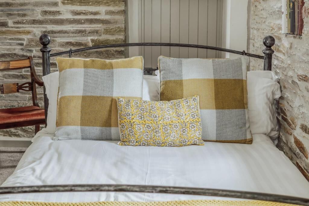 Una cama con estructura metálica, dos almohadas estampadas con cuadros y una alfombra tejida.