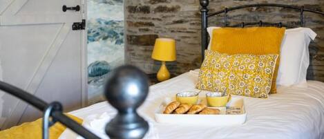 A bed with a tray of pastries, a yellow pillow, and a lamp on a nightstand.
