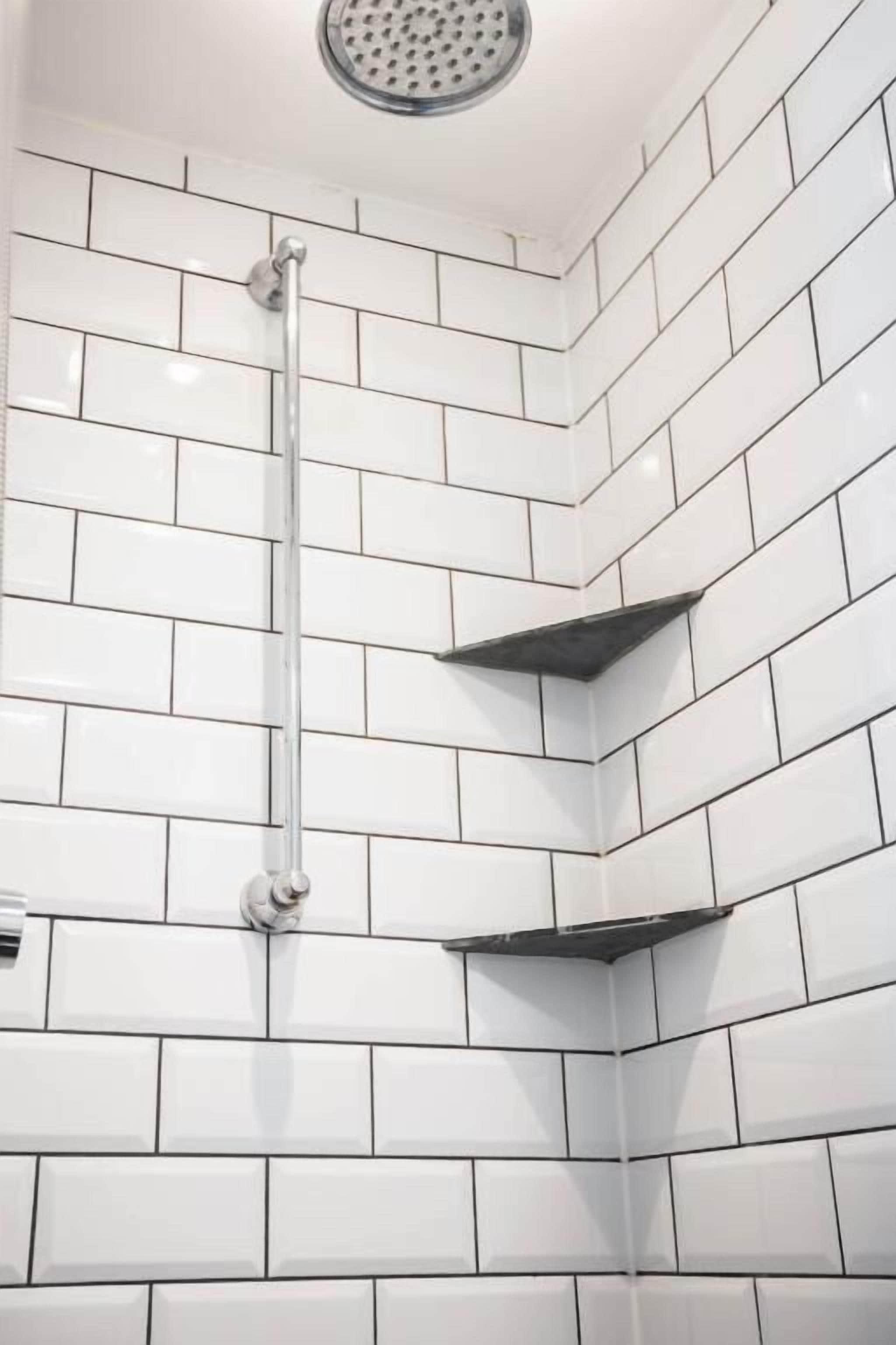 A corner of a room with white tiled walls and a shower area.
