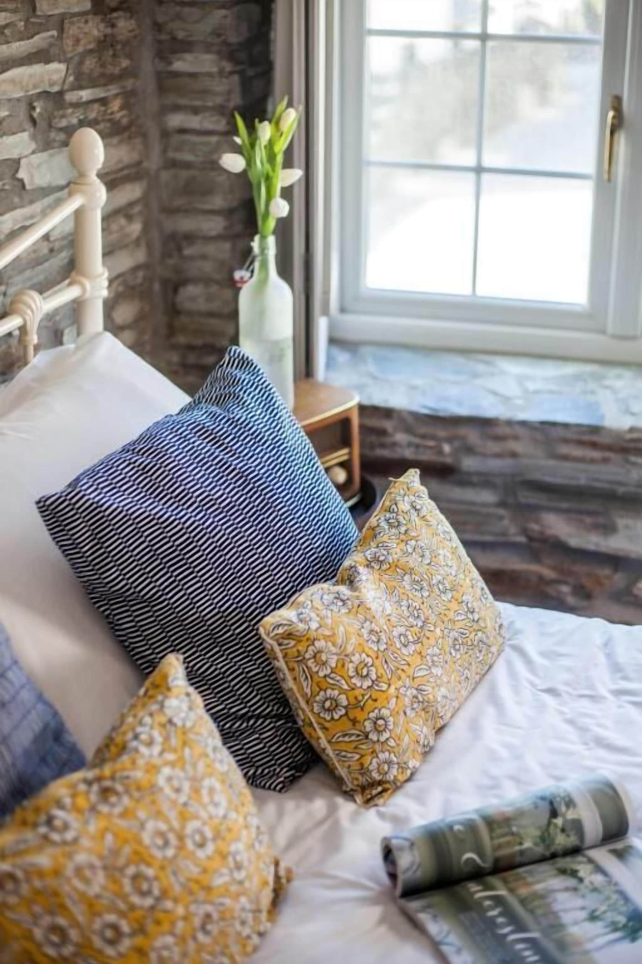 Una cama con almohadas estampadas, un florero con flores y una ventana con vistas.