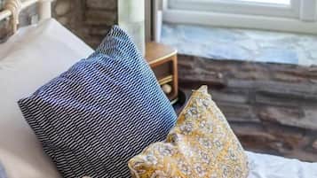 A bed with patterned pillows, a vase with flowers, and a window with a view.