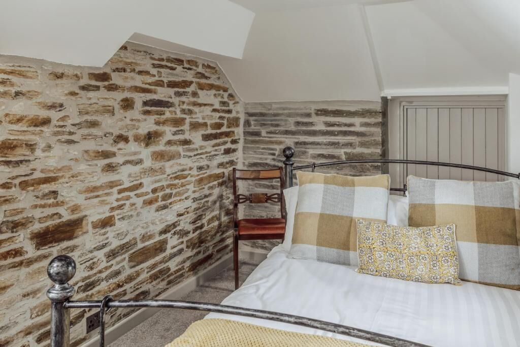 Ein Schlafzimmer mit einer Steinwand, einem Metallbettgestell, einem Holzstuhl und einem gemusterten Kissen.
