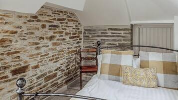 Ein Schlafzimmer mit einer Steinwand, einem Metallbettgestell, einem Holzstuhl und einem gemusterten Kissen.