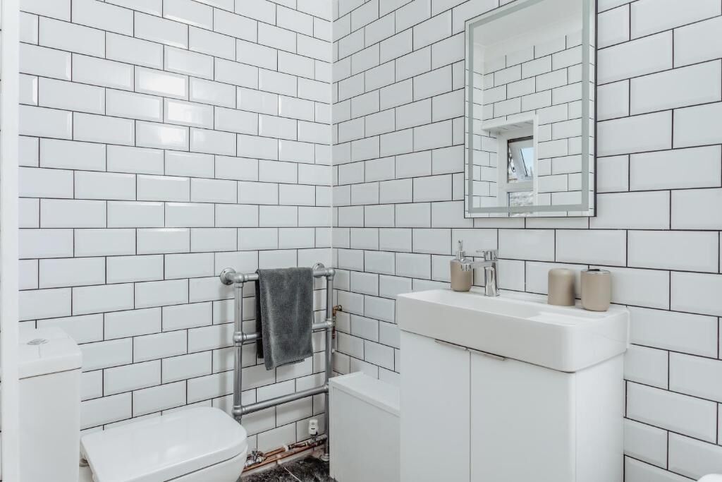 Een badkamer met witte betegeling, een toilet, een wastafel met spiegel en een handdoekrek.