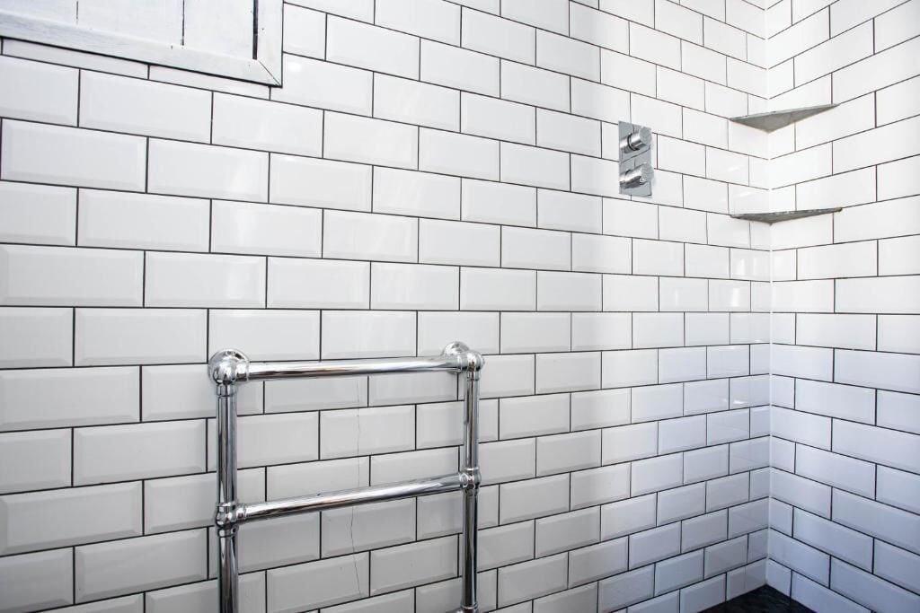A corner of a room with white tiled walls and a metal towel rack.