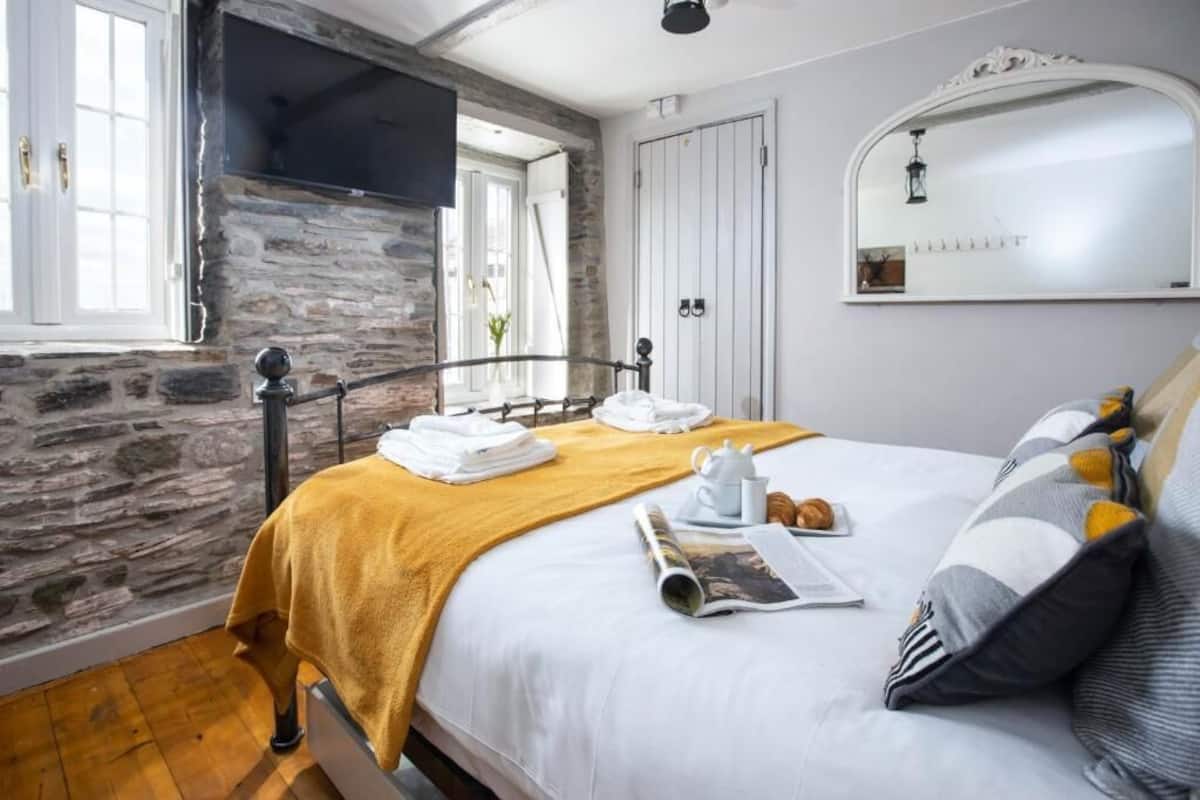 Un dormitorio con pared de piedra, cama con manta amarilla, puerta blanca y espejo.