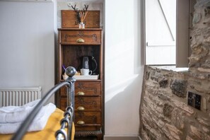 Huoneessa on sänky, puinen lipasto, kiviseinä ja ikkuna.