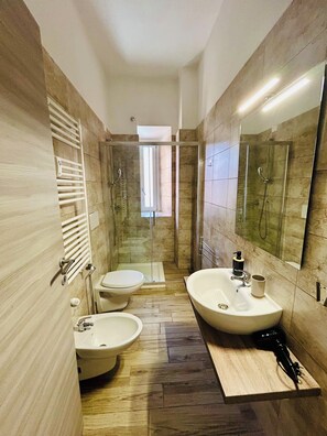 Een moderne badkamer met een douche, twee wastafels, een toilet en een badmeubel.