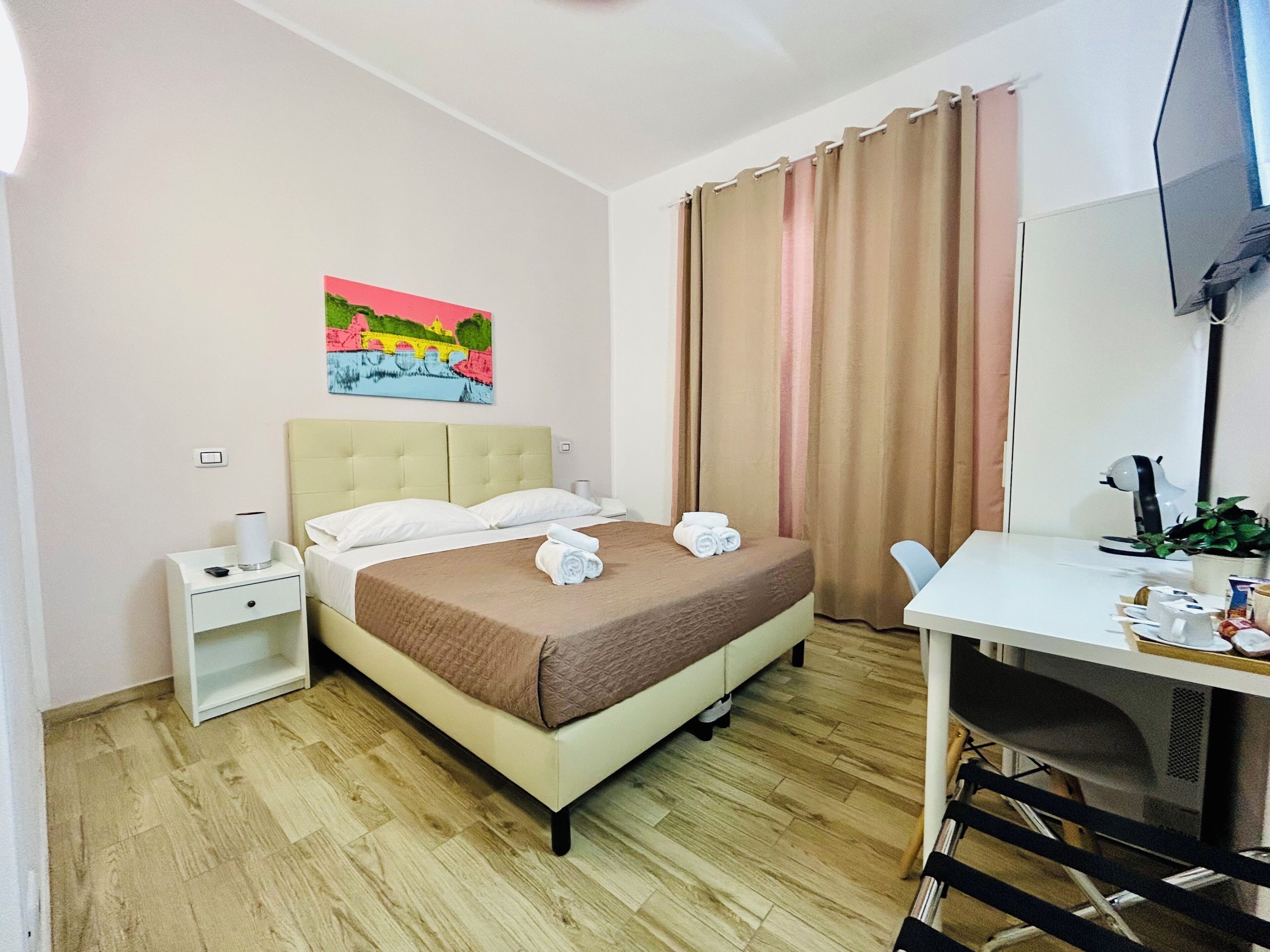 Hotelkamer met een bed, een bureau, een stoel, een televisie, een schilderij aan de muur en een raam met gordijnen.