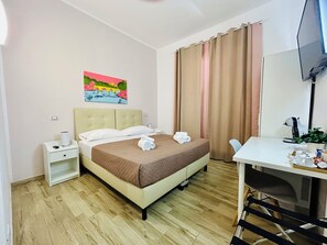 Hotelkamer met een bed, een bureau, een stoel, een televisie, een schilderij aan de muur en een raam met gordijnen.
