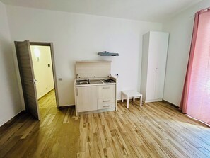 Ein kleiner, offener Raum mit Küchenzeile, einem einzelnen weißen Schrank, einem kleinen weißen Tisch und einem Kleiderschrank.