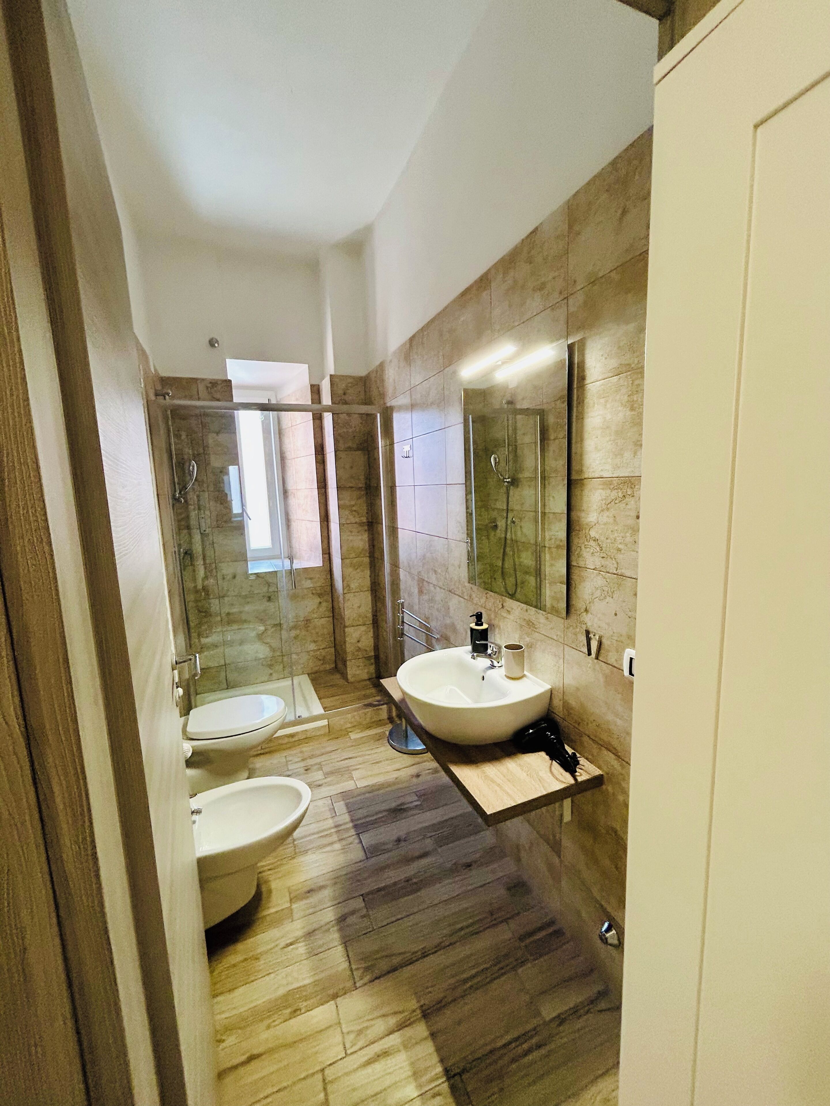 Un baño con ducha, dos inodoros, un lavabo y un espejo.