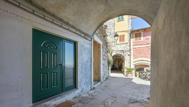 Un callejón estrecho con una puerta verde, un camino de adoquines y edificios de piedra con arcos.