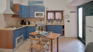 Una cocina compacta con armarios azules, estufa, microondas y una mesa de comedor con sillas.