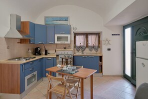 Eine kleine Küche mit blauen Schränken, einem Herd, einer Mikrowelle und einem Esstisch mit Stühlen.