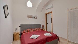 Un dormitorio con cama, mesita de noche, lámpara, un cuadro en la pared y un equipo de aire acondicionado.