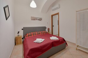 Ein Schlafzimmer mit einem Bett, einem Nachttisch, einer Lampe, einem Bild an der Wand und einer Klimaanlage.