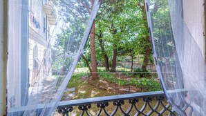 Blick durch ein Maschengitter auf einen Garten mit Bäumen und ein Gebäude im Hintergrund.
