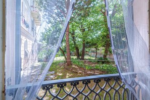 Blick durch ein Maschengitter auf einen Garten mit Bäumen und ein Gebäude im Hintergrund.