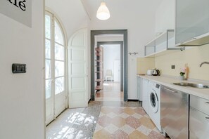 Ein schmaler Flur mit einer Tür zu einem Waschraum, einer Waschmaschine und einer Küche mit Spüle und Arbeitsplatte.