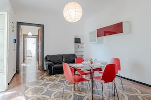 Zona pranzo con tavolo in vetro, sedie rosse, divano in pelle nera, pavimento decorato e lampadario.
