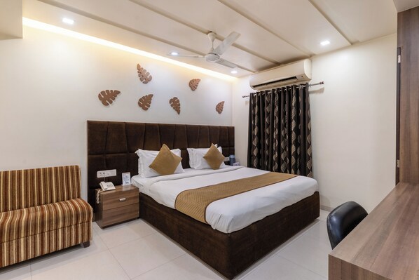 A hotel room with a bed, bedside table, chair, and a desk. - HOTEL ASHISH (Ahmedabad)