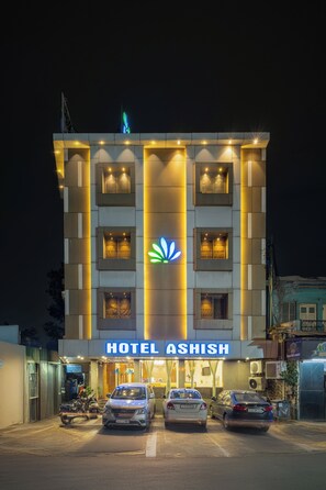 A hotel with a prominent sign, multiple cars parked in front, and a well-lit facade. - HOTEL ASHISH (Ahmedabad)