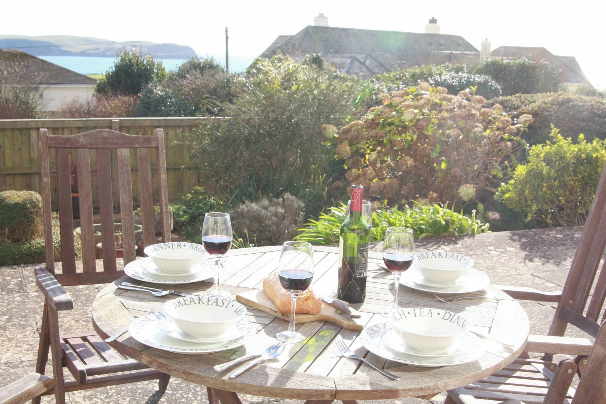 A wooden table set for breakfast and dinner with wine glasses, a bottle, and bread.
