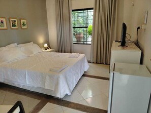 Quarto de hotel com uma cama, uma mesa, uma televisão e uma janela com cortinas.