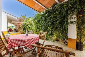 Une terrasse extérieure avec une nappe à carreaux, des chaises en bois et une bouteille de vin.