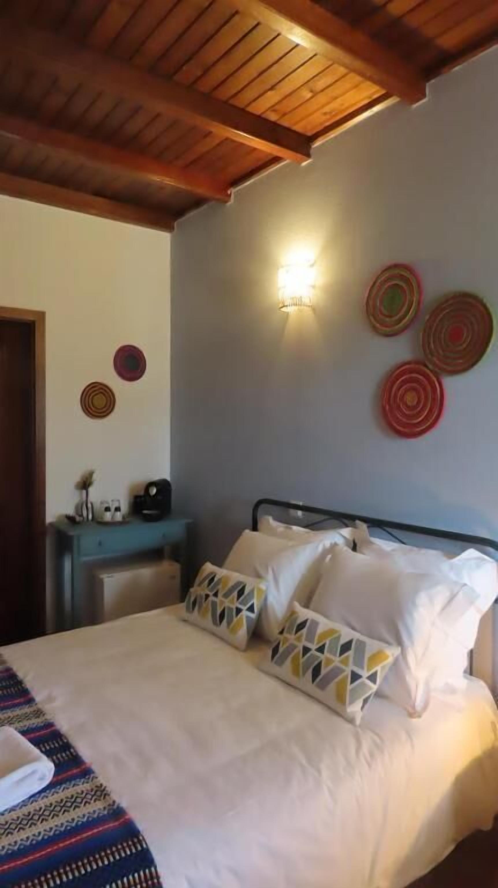 Quarto com cama, almofadas, mesa de cabeceira, luminária na parede e pratos decorativos.