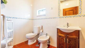 A bathroom with white tiles, a wooden cabinet, a sink, a toilet, and a bidet.