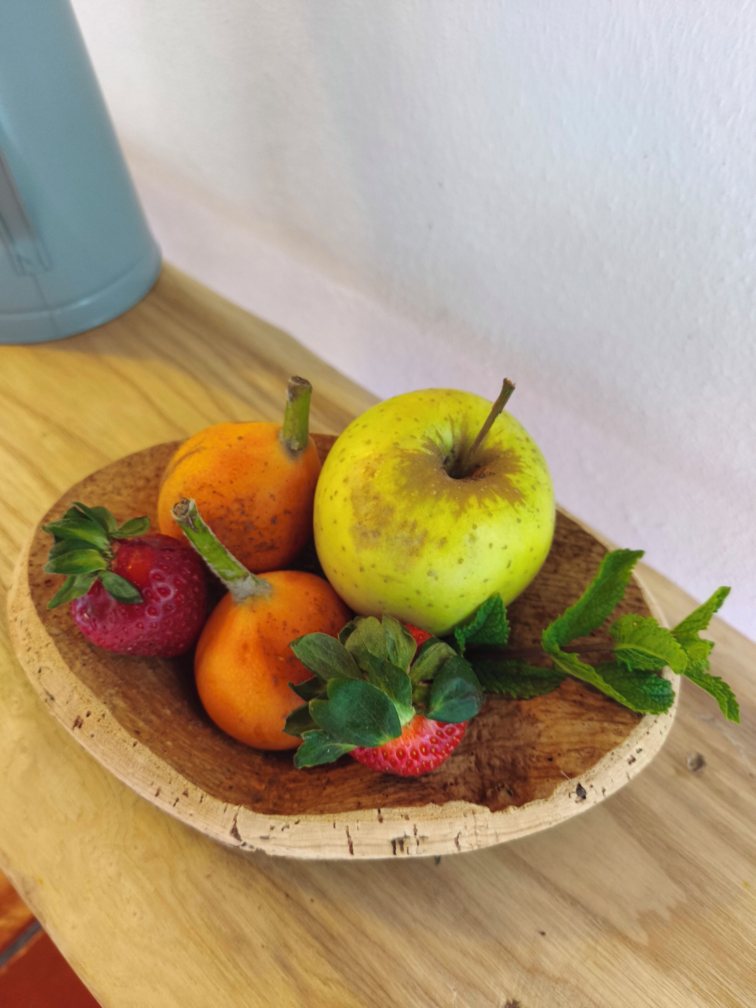 Una bandeja de madera con fresas, una manzana y una naranja.