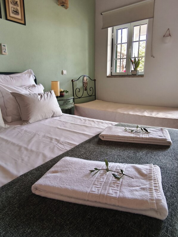 A bedroom with two beds, a window with a view, a bedside table with a lamp, and a wall clock.