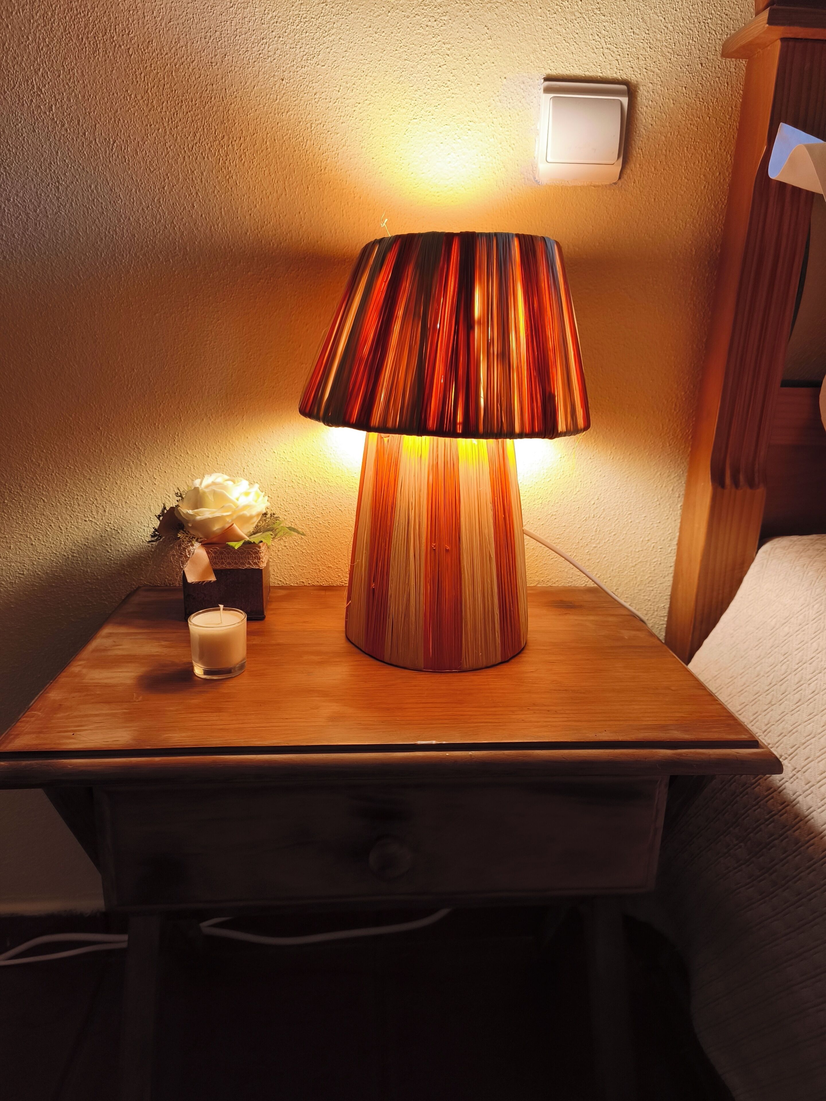 Une table de chevet en bois, avec une lampe, une bougie et une petite plante.