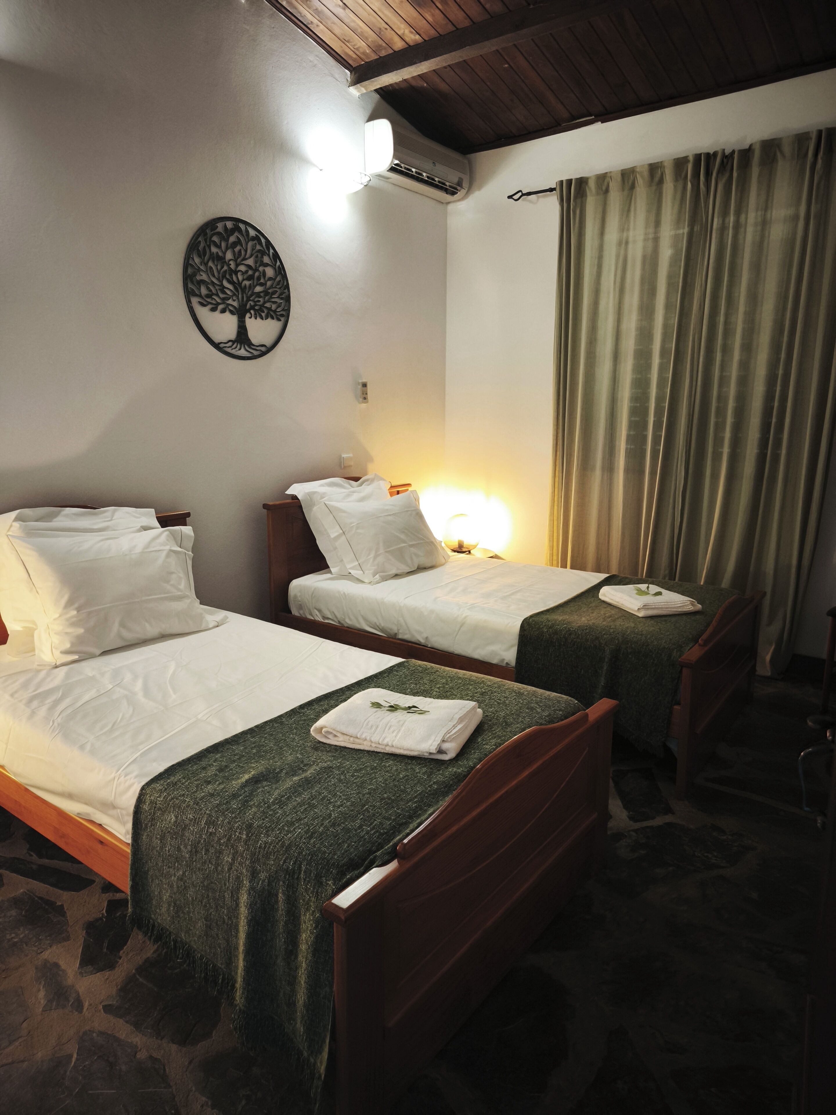 Une chambre avec deux lits, un climatiseur fixé au mur, un arbre décoratif, une lampe et un rideau.