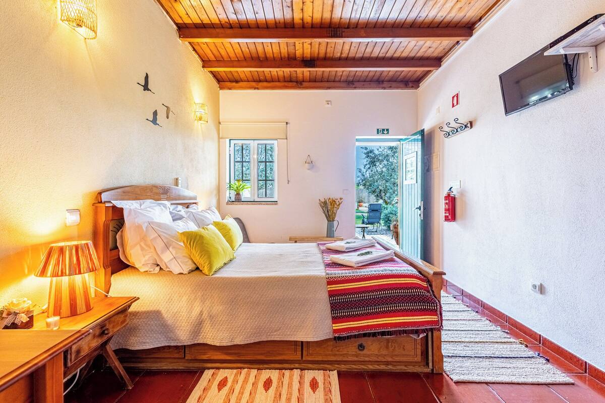A bedroom with a wooden bed, a nightstand, a lamp, a window, and a view of the outside.
