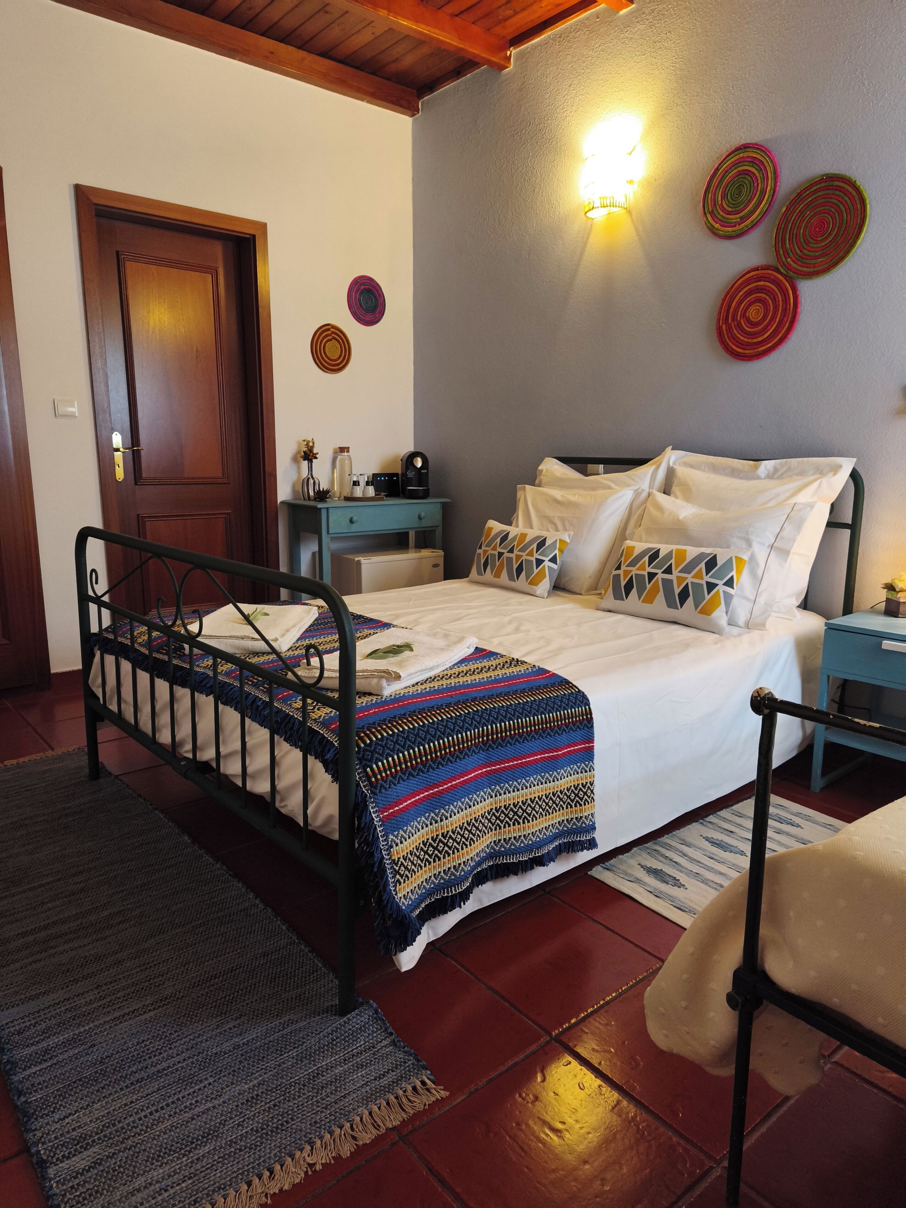 A bedroom with a bed, bedside tables, a nightstand, a wooden door, and a wall-mounted light fixture.
