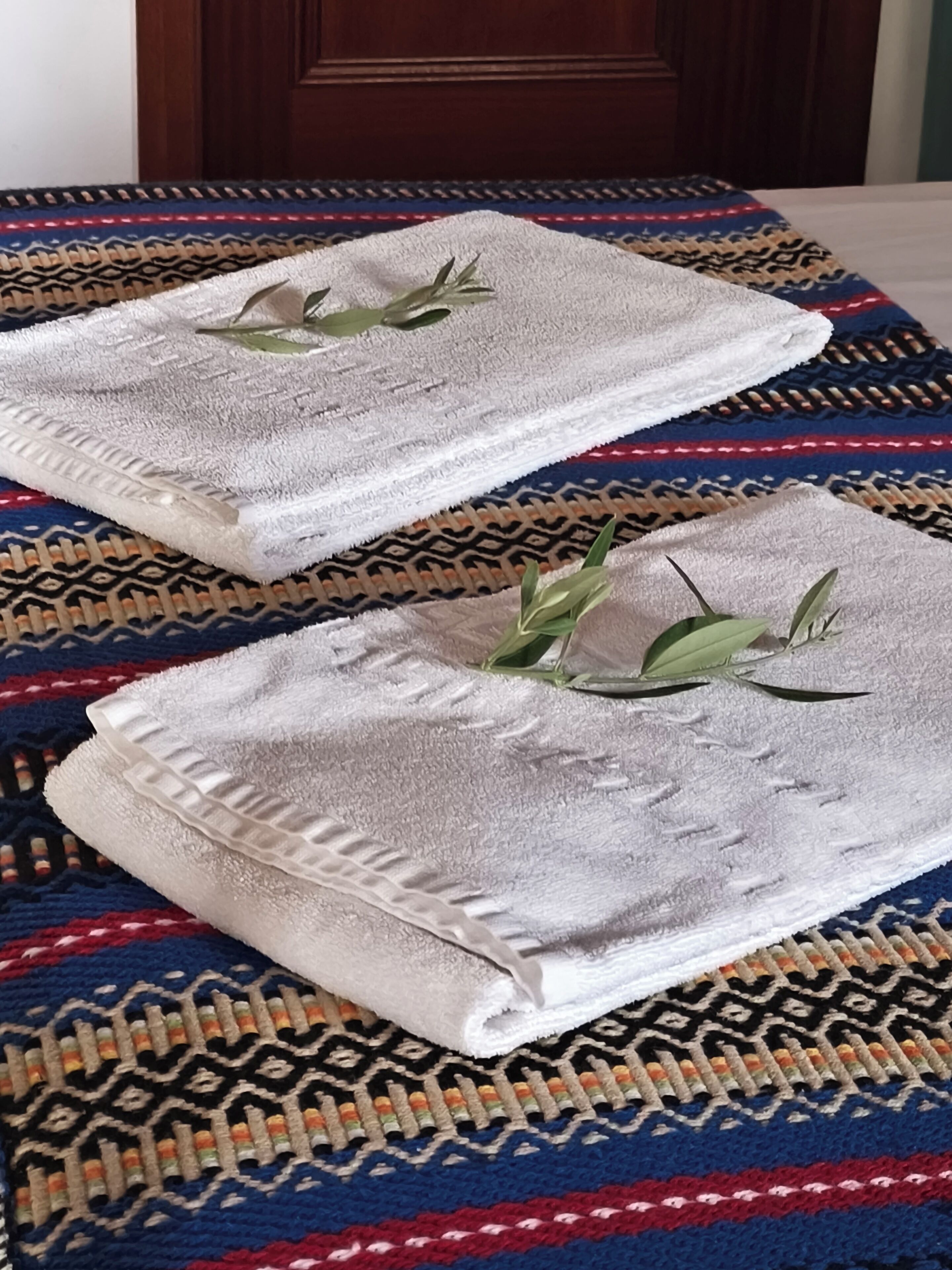Two neatly folded towels with a leaf decoration on a patterned rug.