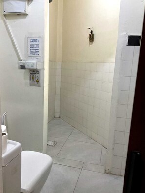 Et lille badeværelse med toilet, brusekabine og et skilt, der beder om ikke at skylle papirhåndklæder.