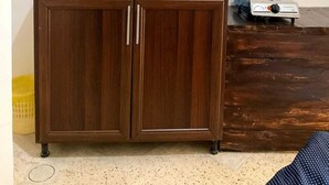 Une cuisine avec des meubles en bois, un évier en acier inoxydable, une cuisinière à gaz et une fenêtre ornée d’un rideau violet.