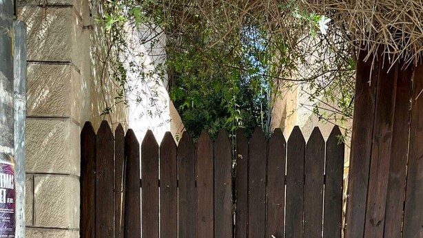 Une porte en bois, dotée d’un loquet métallique, est intégrée à un mur de pierre, et un chemin pavé de briques mène à cette porte.