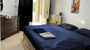 Une chambre à coucher comprenant un lit, une commode, un tableau et une porte donnant sur un espace extérieur.