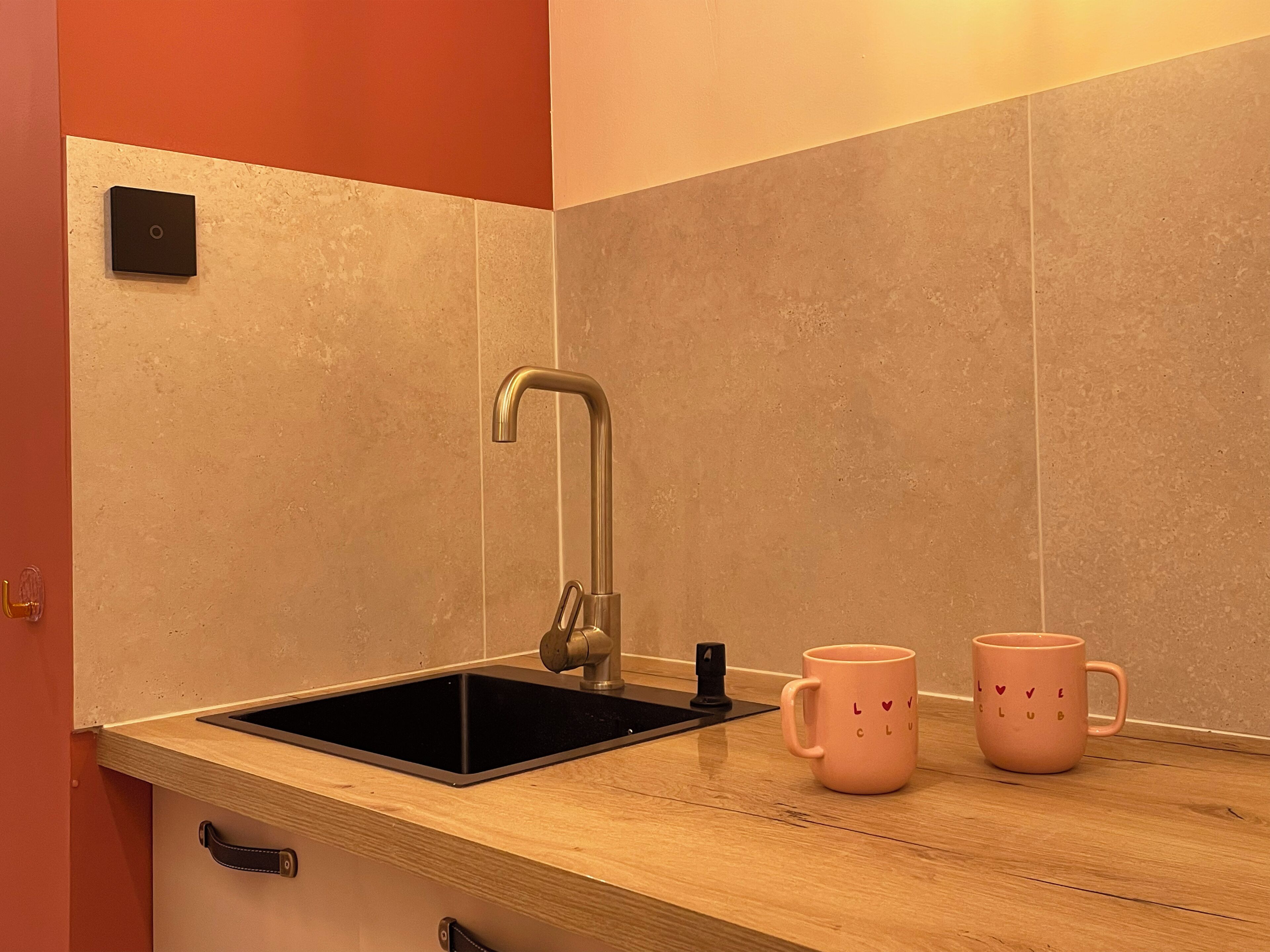 A kitchen with a black sink, stainless steel faucet, and two pink mugs on the counter.