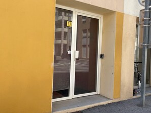 En byggnadsingång med en glasdörr, en gul vägg och en metallkonstruktion till höger.