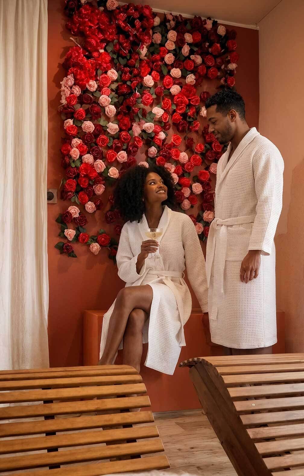 Une pièce dont un mur est décoré de roses rouges et roses, avec un banc en bois et une personne vêtue d’une robe blanche.