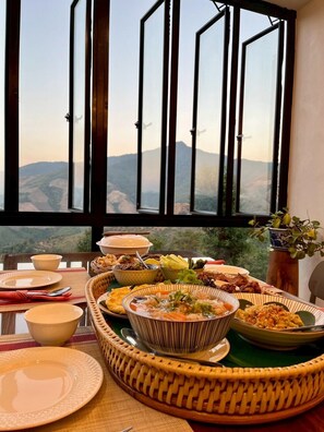 A dining table with various dishes and a view of mountains through large windows. - Mei Nai Home (Pua)